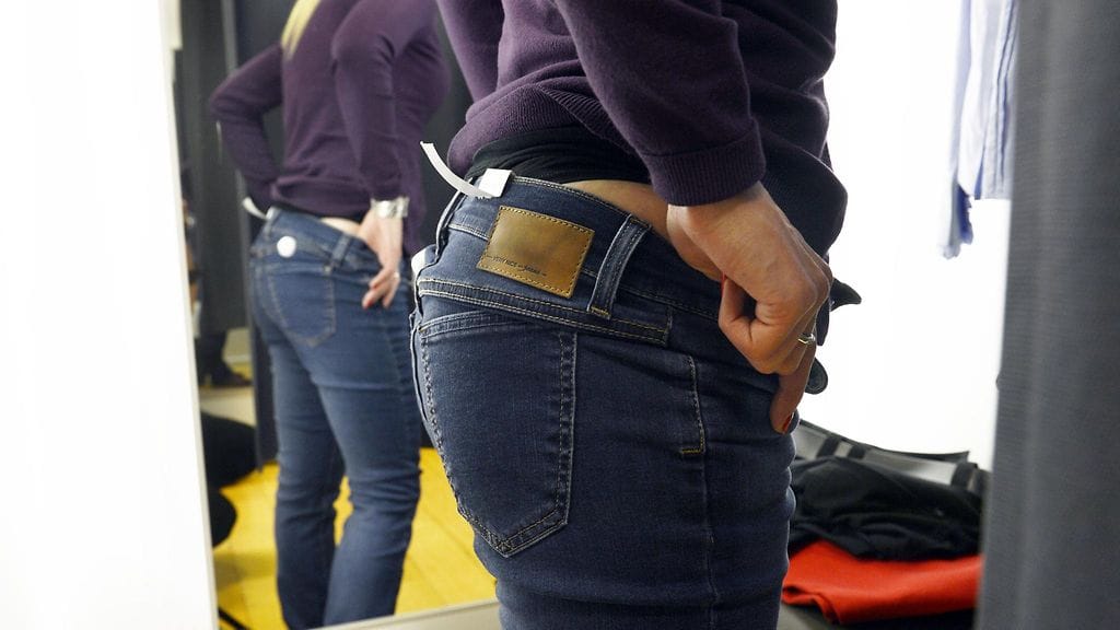 Nainen puki liikkeen sovituskopissa ylleen legginsit, joiden päälle hän puki omat housunsa. Kuvituskuva.